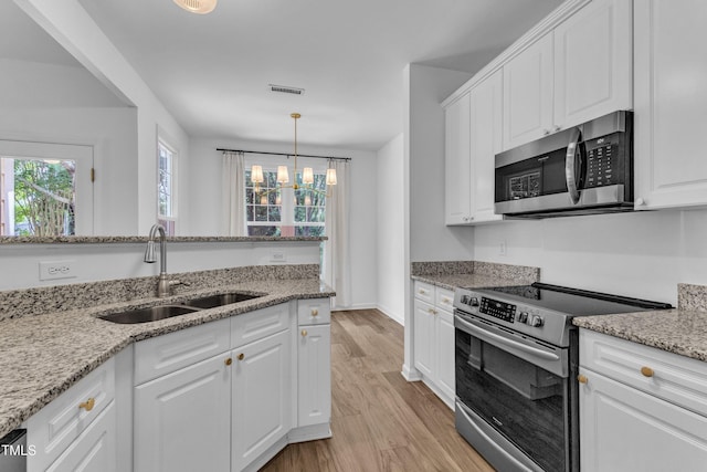 kitchen with appliances with stainless steel finishes, a sink, light wood finished floors, a chandelier, and white cabinetry
