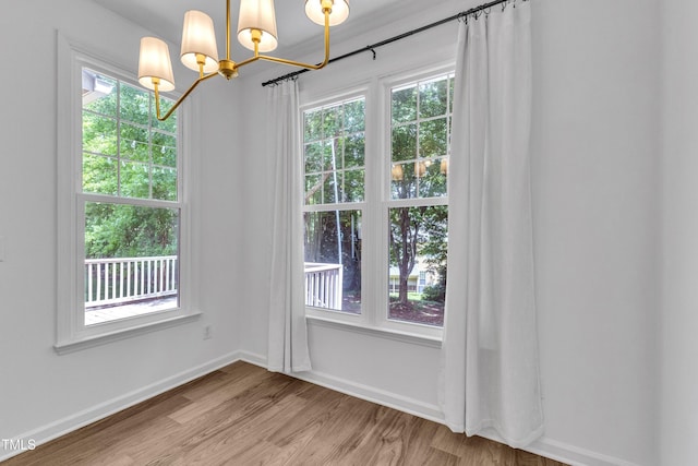 unfurnished dining area featuring a chandelier, light wood-type flooring, and baseboards