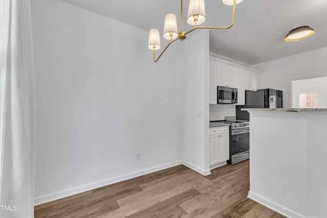 kitchen featuring stainless steel appliances, wood finished floors, white cabinetry, a chandelier, and light stone countertops