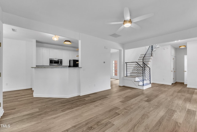 unfurnished living room featuring stairs, light wood-style flooring, a ceiling fan, and baseboards