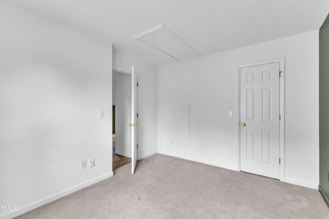 empty room with attic access, carpet flooring, and baseboards