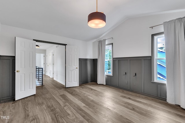 unfurnished bedroom with wood finished floors, a wainscoted wall, a decorative wall, and lofted ceiling