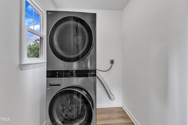 laundry room with stacked washer / dryer, wood finished floors, and baseboards