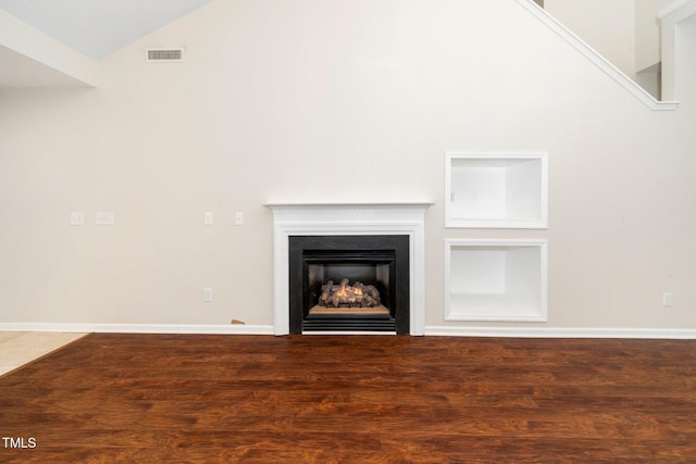 unfurnished living room featuring wood finished floors, lofted ceiling, a warm lit fireplace, and baseboards
