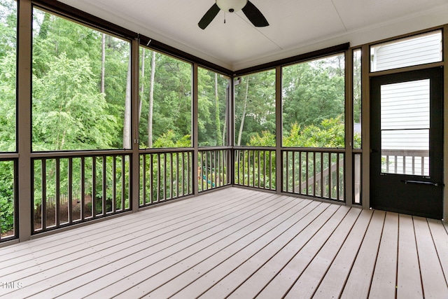unfurnished sunroom featuring ceiling fan and a wooded view