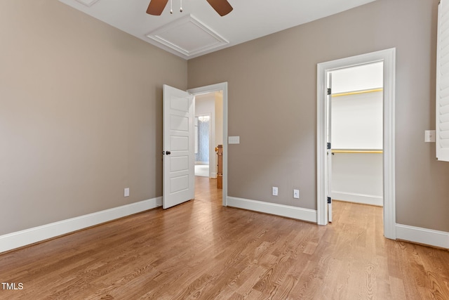 unfurnished bedroom featuring attic access, light wood finished floors, baseboards, and a spacious closet