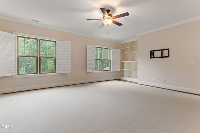 empty room featuring plenty of natural light, ornamental molding, a ceiling fan, built in shelves, and baseboards