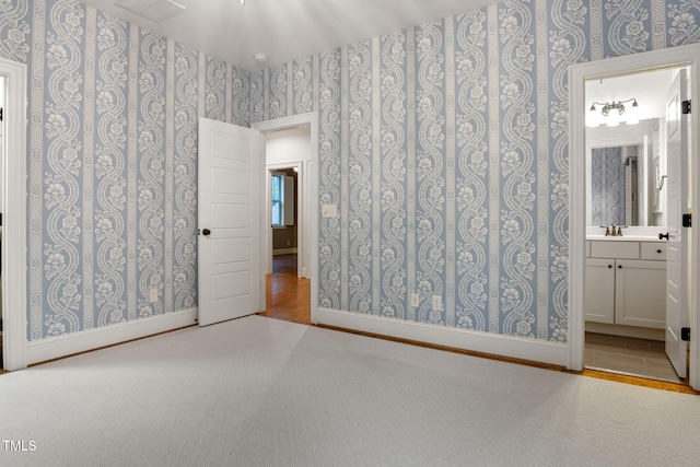unfurnished bedroom featuring wallpapered walls, a sink, connected bathroom, and baseboards