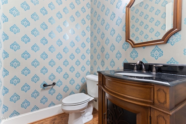 half bath with wallpapered walls, toilet, baseboards, vanity, and wood finished floors