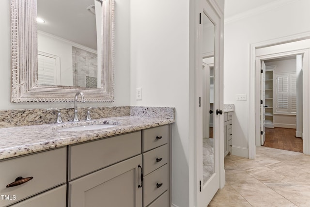 full bath featuring ornamental molding, vanity, tiled shower, and baseboards
