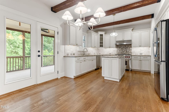 kitchen featuring appliances with stainless steel finishes, under cabinet range hood, a sink, healthy amount of natural light, and beamed ceiling