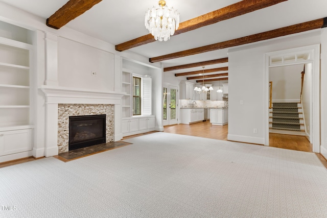 unfurnished living room with a chandelier, a tile fireplace, stairs, beamed ceiling, and a sink