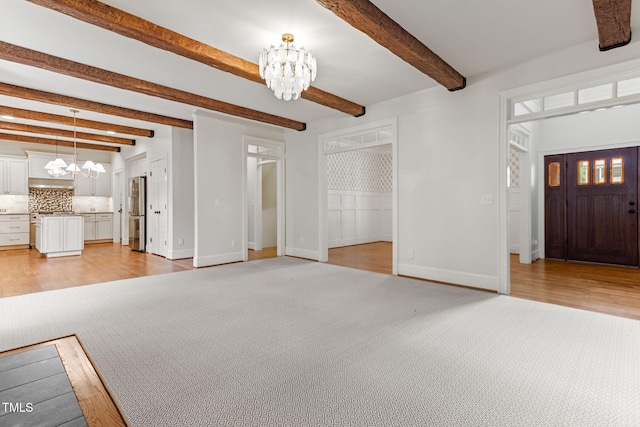 entrance foyer featuring a chandelier, light wood finished floors, beam ceiling, baseboards, and light carpet