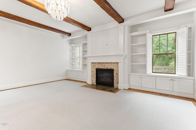 unfurnished living room with beam ceiling, a chandelier, a fireplace, baseboards, and wood finished floors