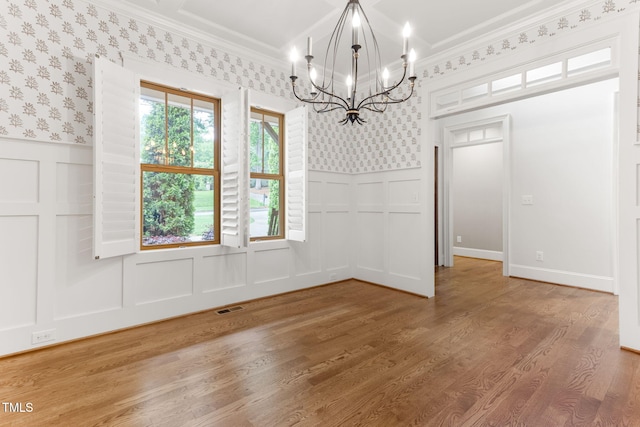 unfurnished dining area with a decorative wall, a chandelier, ornamental molding, a wainscoted wall, and wood finished floors
