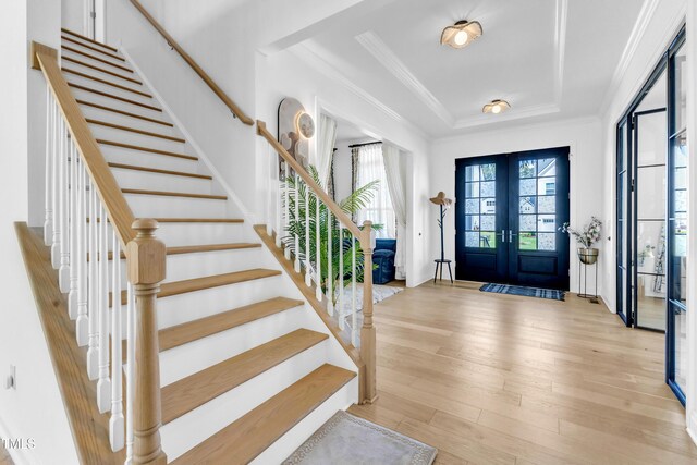 foyer entrance featuring stairs, light wood-style flooring, a raised ceiling, french doors, and crown molding