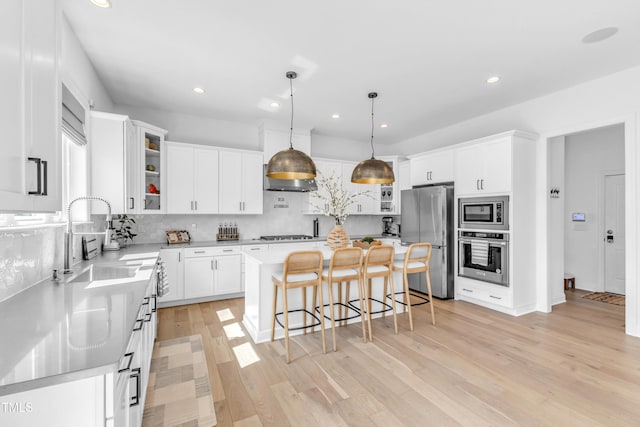 kitchen featuring stainless steel appliances, a sink, a breakfast bar, tasteful backsplash, and light wood-style flooring