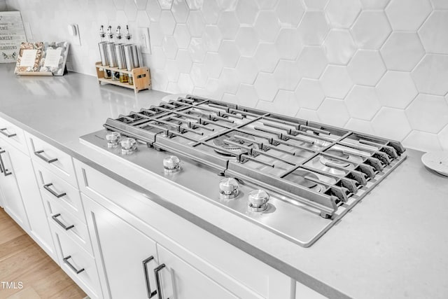 kitchen view of stainless steel gas cooktop, backsplash, white cabinets, light countertops, and light wood-type flooring