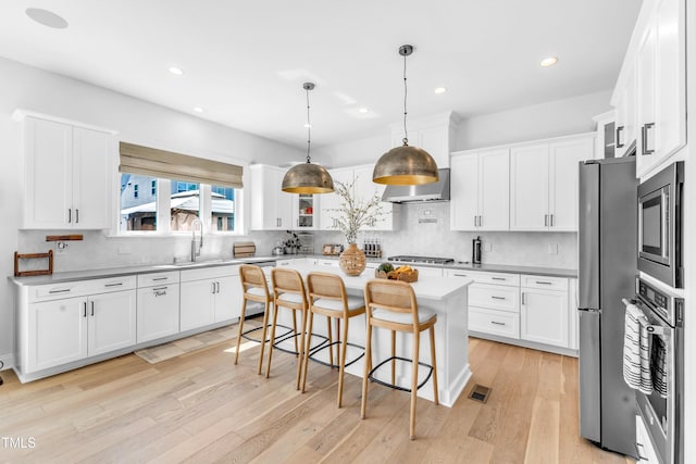 kitchen with stainless steel appliances, a sink, wall chimney exhaust hood, a kitchen bar, and white cabinets