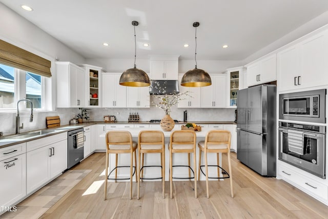 kitchen featuring appliances with stainless steel finishes, a sink, glass insert cabinets, light wood-style floors, and white cabinetry