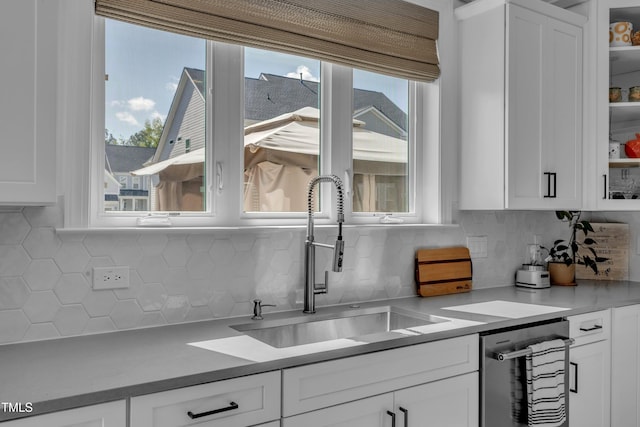 kitchen featuring a sink, dishwasher, decorative backsplash, and white cabinetry