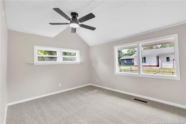 carpeted empty room with healthy amount of natural light, ceiling fan, baseboards, lofted ceiling, and a textured ceiling