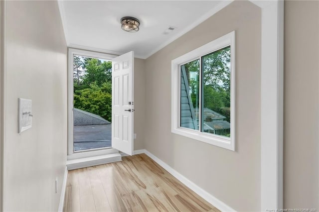 doorway with healthy amount of natural light, light wood-type flooring, baseboards, and ornamental molding
