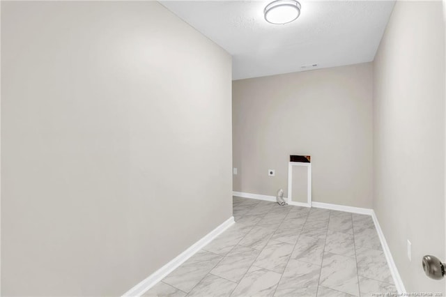 spare room featuring light marble finish floors, baseboards, and a textured ceiling