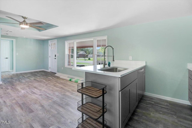 kitchen with a sink, ceiling fan, light countertops, baseboards, and dark wood-style flooring