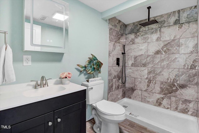 bathroom featuring toilet, vanity, wood finished floors, and tiled shower