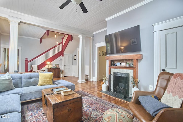 living room featuring decorative columns, stairs, wood finished floors, a ceiling fan, and ornamental molding