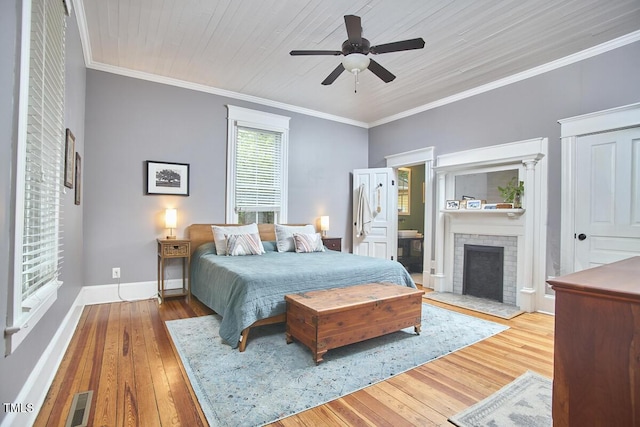 bedroom with wood-type flooring, a brick fireplace, ornamental molding, baseboards, and ceiling fan