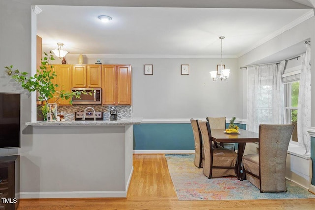 dining room with light wood-type flooring, a chandelier, ornamental molding, and baseboards