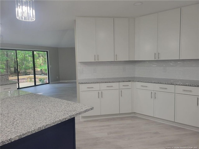 kitchen featuring tasteful backsplash, white cabinets, light stone countertops, light wood-style floors, and baseboards