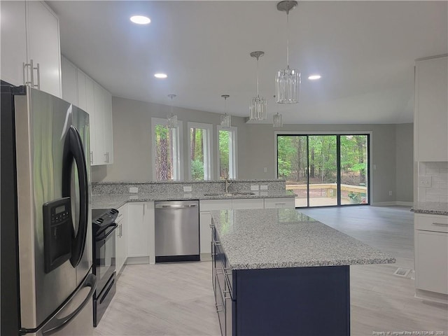 kitchen featuring appliances with stainless steel finishes, a sink, light wood finished floors, a peninsula, and white cabinetry