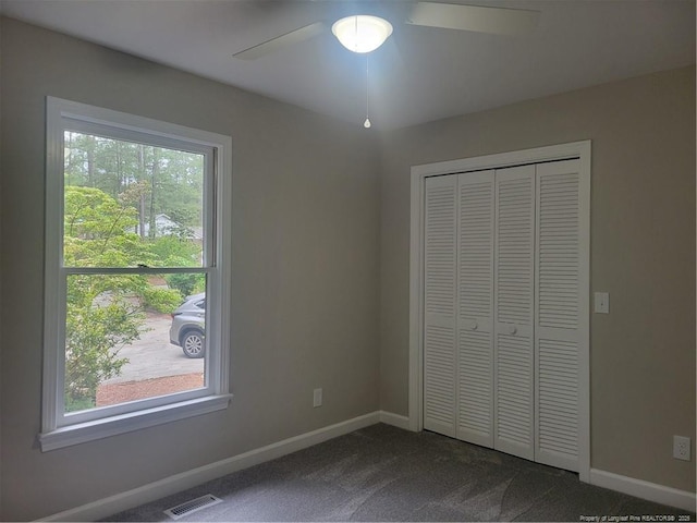 unfurnished bedroom featuring dark colored carpet, multiple windows, and baseboards