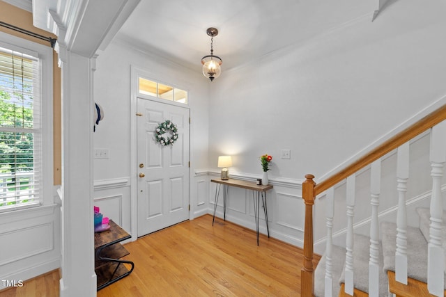 foyer entrance with healthy amount of natural light, a wainscoted wall, light wood-style floors, ornamental molding, and a decorative wall