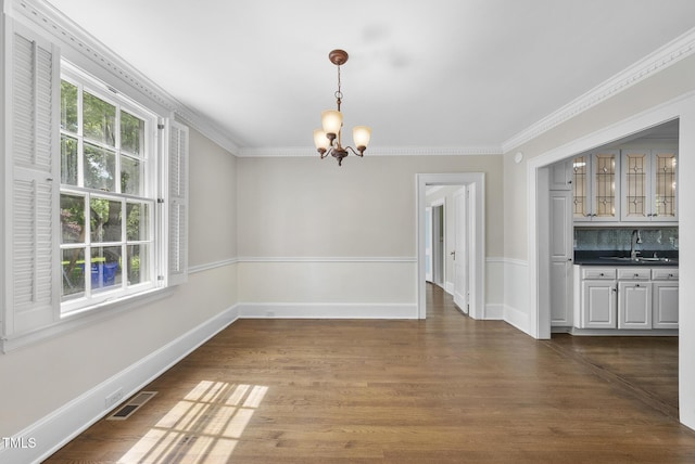 unfurnished dining area featuring a chandelier, a sink, ornamental molding, wood finished floors, and baseboards