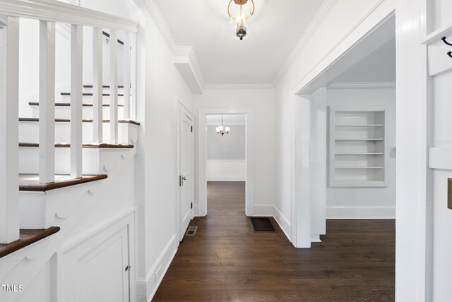 hall featuring dark wood finished floors, ornamental molding, baseboards, a chandelier, and built in shelves