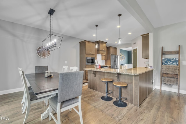 1109 Agio Ct, Zebulon, NC 27597 - kitchen featuring appliances with stainless steel finishes, light stone counters, light wood-style floors, baseboards, and a peninsula
