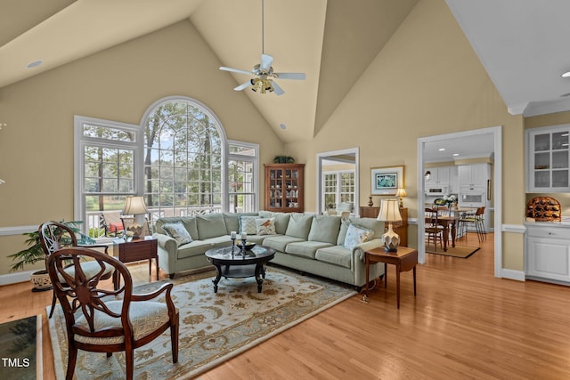 living area with high vaulted ceiling, a ceiling fan, light wood-type flooring, recessed lighting, and baseboards