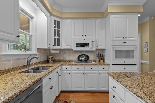 kitchen with white appliances, a sink, crown molding, white cabinetry, and light stone counters