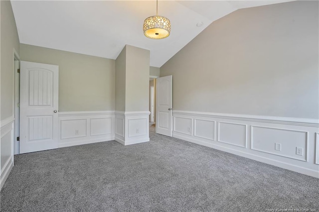 spare room with vaulted ceiling, carpet, wainscoting, and a decorative wall