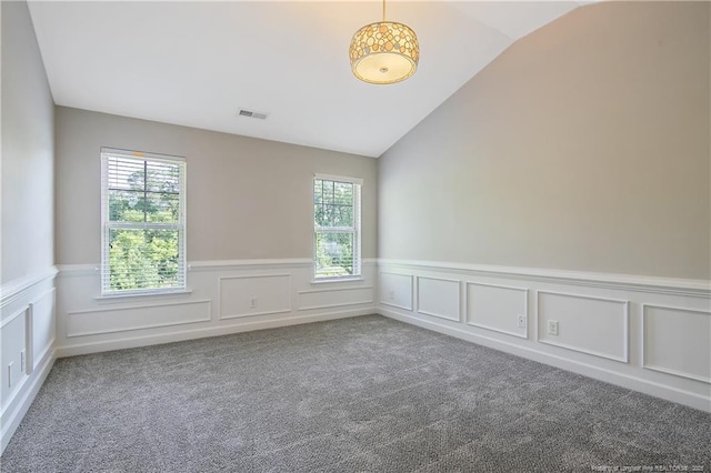 carpeted empty room with lofted ceiling, plenty of natural light, wainscoting, and a decorative wall