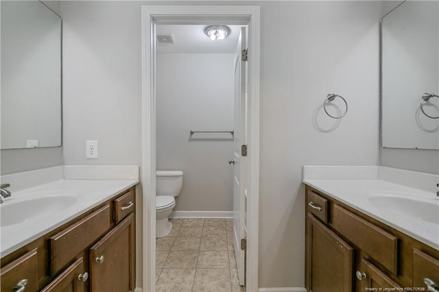 bathroom featuring toilet, two vanities, and baseboards