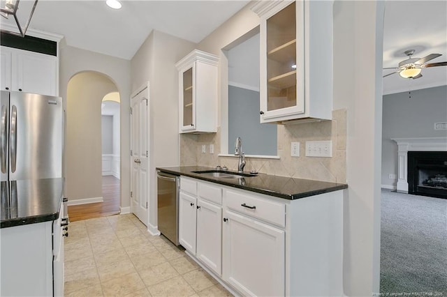 kitchen with a sink, stainless steel appliances, ceiling fan, arched walkways, and glass insert cabinets