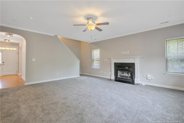 unfurnished living room with carpet flooring, a ceiling fan, ornamental molding, baseboards, and a high end fireplace