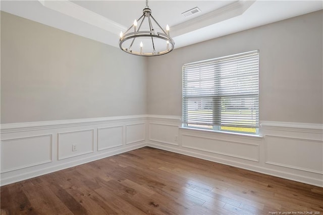 spare room with a chandelier, a raised ceiling, crown molding, a wainscoted wall, and hardwood / wood-style floors