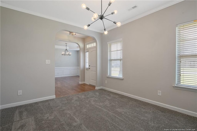 spare room featuring a chandelier, arched walkways, carpet, ornamental molding, and baseboards