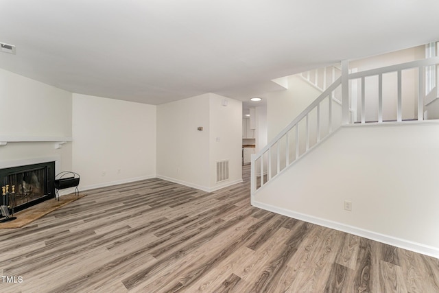 unfurnished living room featuring stairway, wood finished floors, baseboards, and a fireplace with flush hearth